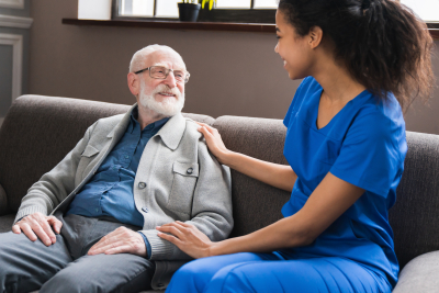 Caring african nurse talks to old patient grandfather holds his hand sit in living room at homecare visit provide psychological support listen complains showing empathy encouraging, caregiving concept